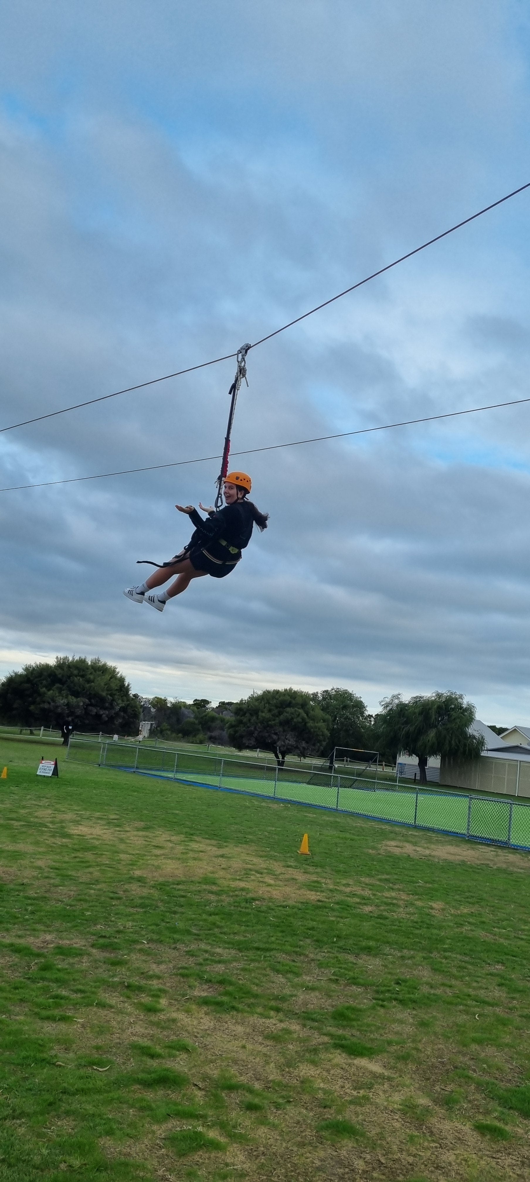 A child wearing a helmet and harness gliding on a zip line over a grass field